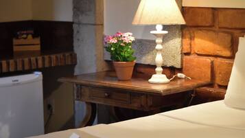 Habitación de hotel con cama, mesita de noche con lámpara, planta en maceta y un refrigerador pequeño.