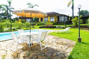 A pool area with stone flooring, a white table with chairs, and a yellow umbrella. - Paço do Lavradio Pousada (São João del Rei)