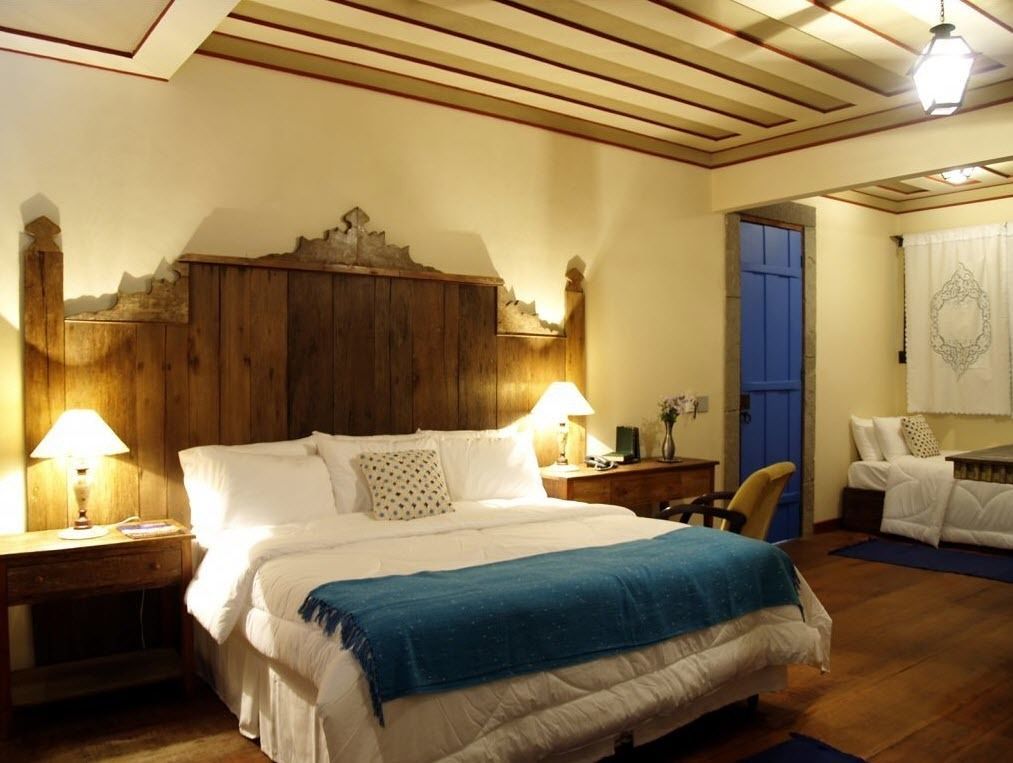 A bedroom with a wooden headboard, two bedside tables with lamps, a bed with white bedding and a blue throw, and a chair.