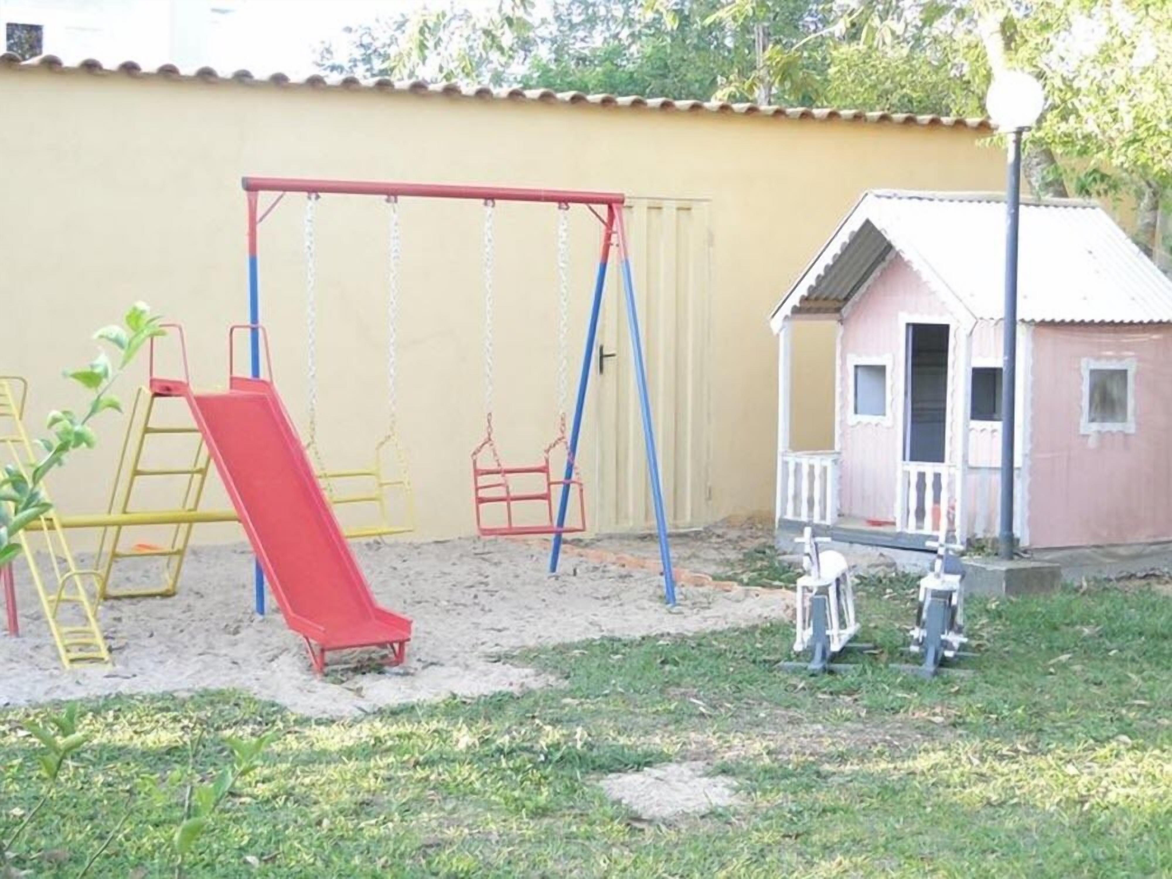 Un parque infantil con columpios y un tobogán, un edificio pequeño y una escalera.
