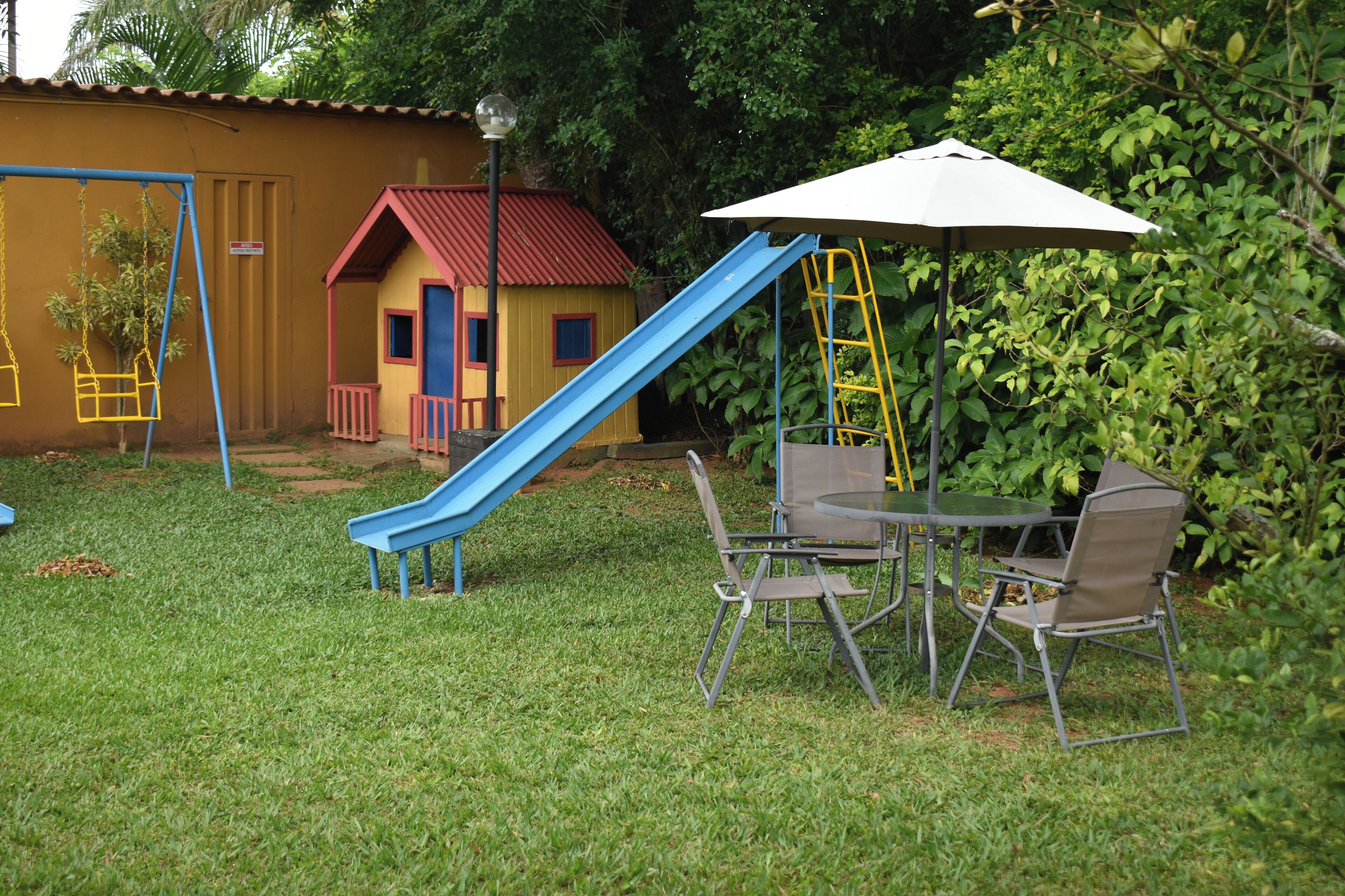 A playground with a blue slide, a small yellow house, and a table with chairs.