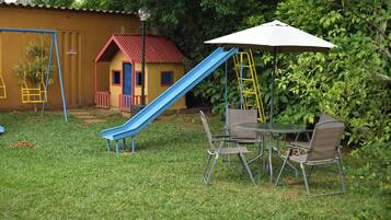 A playground with a blue slide, a small yellow house, and a table with chairs.