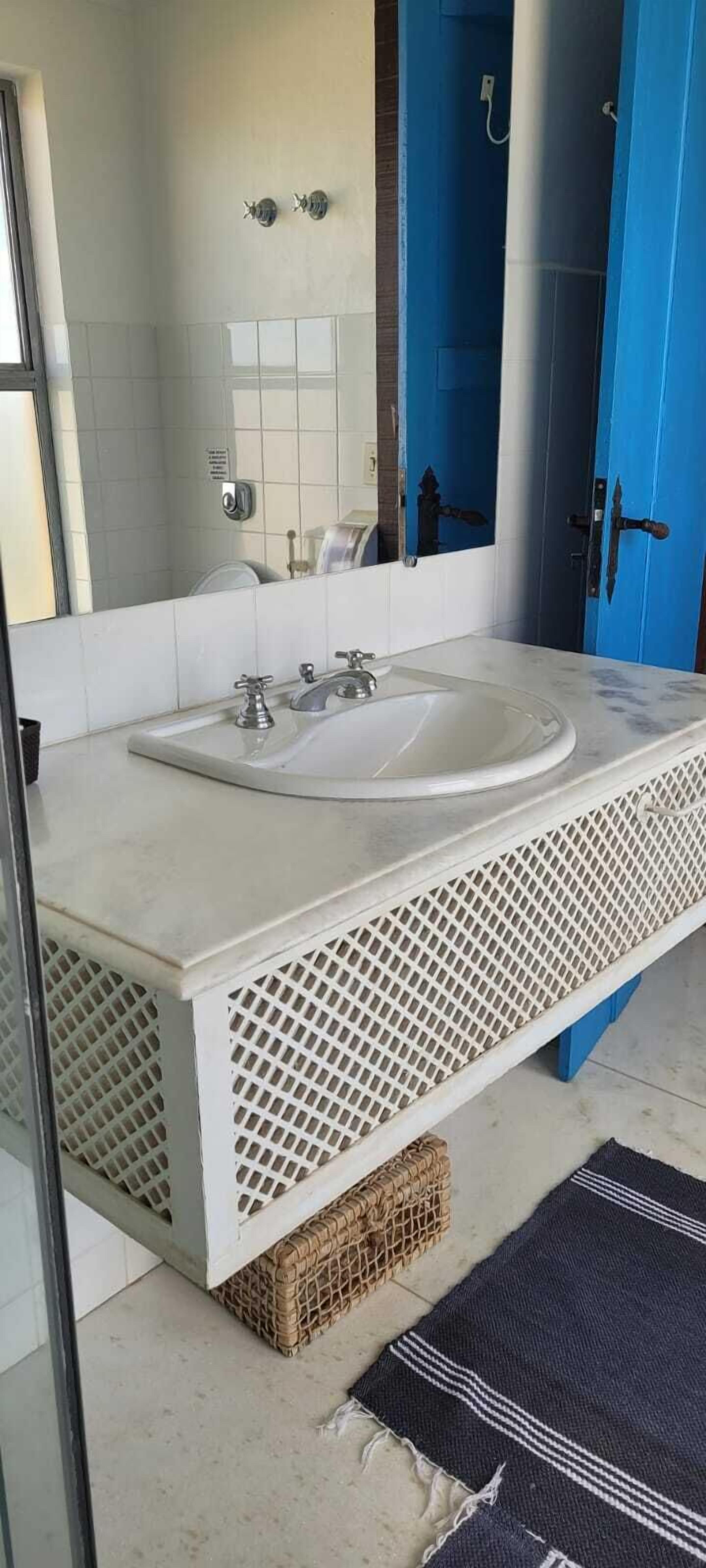 A bathroom with a white sink, blue door, and a large mirror.