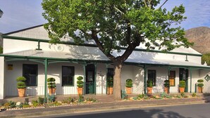 A two-story building with a green roof and white walls, featuring a large tree in front. - Maison Fougere (Franschhoek)