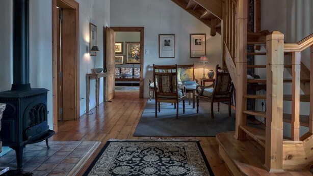 A spacious living area with a wooden staircase, a fireplace, and a dining area with chairs and a table. - Maison Fougere (Franschhoek)