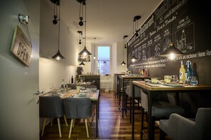 Un espace repas moderne avec une table en bois dressée pour deux personnes, un éclairage suspendu au plafond et un menu écrit à la craie sur le mur.