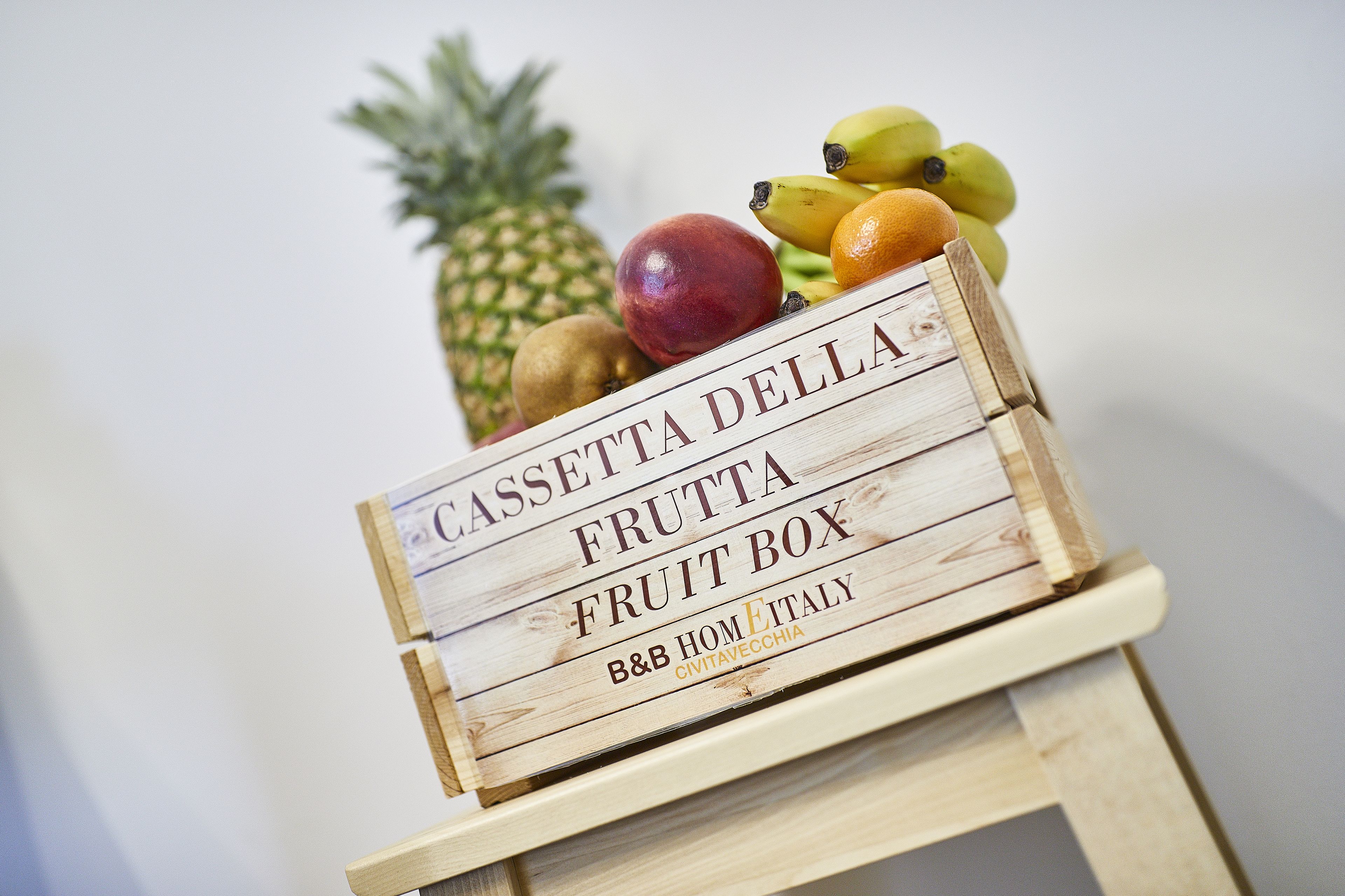 A wooden fruit box labeled "CASSETTA DELLA FRUTTA" with various fruits like bananas, apples, and a pineapple.