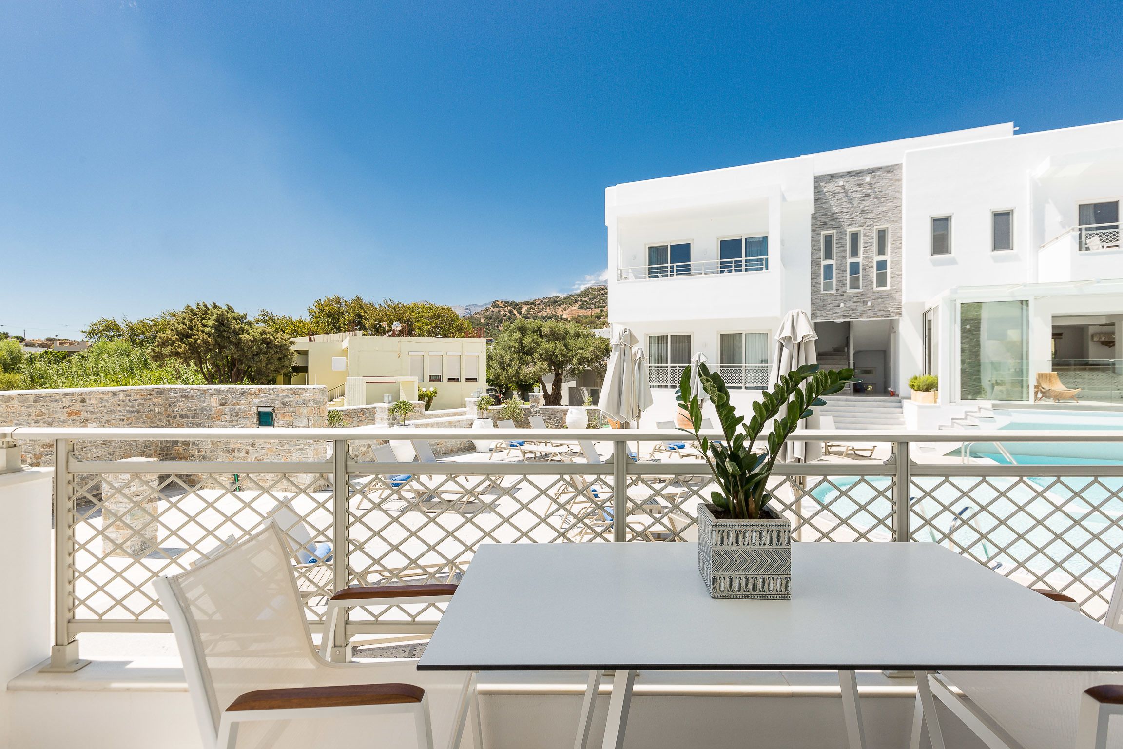 A modern outdoor terrace with a pool, white furniture, and a view of a white building with a stone facade.