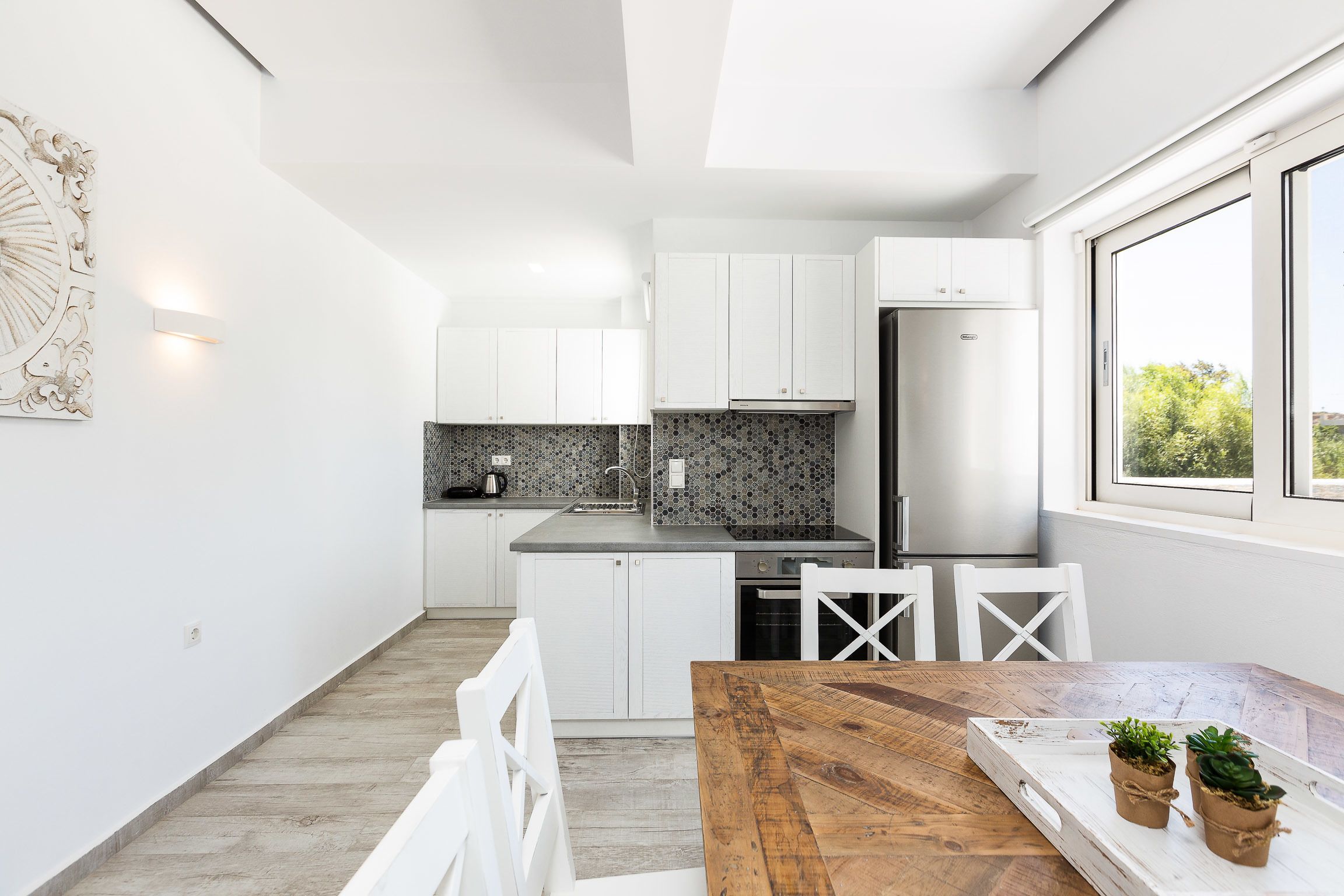 Una cocina moderna con armarios blancos, una mesa de comedor de madera y vistas a zonas verdes al exterior.