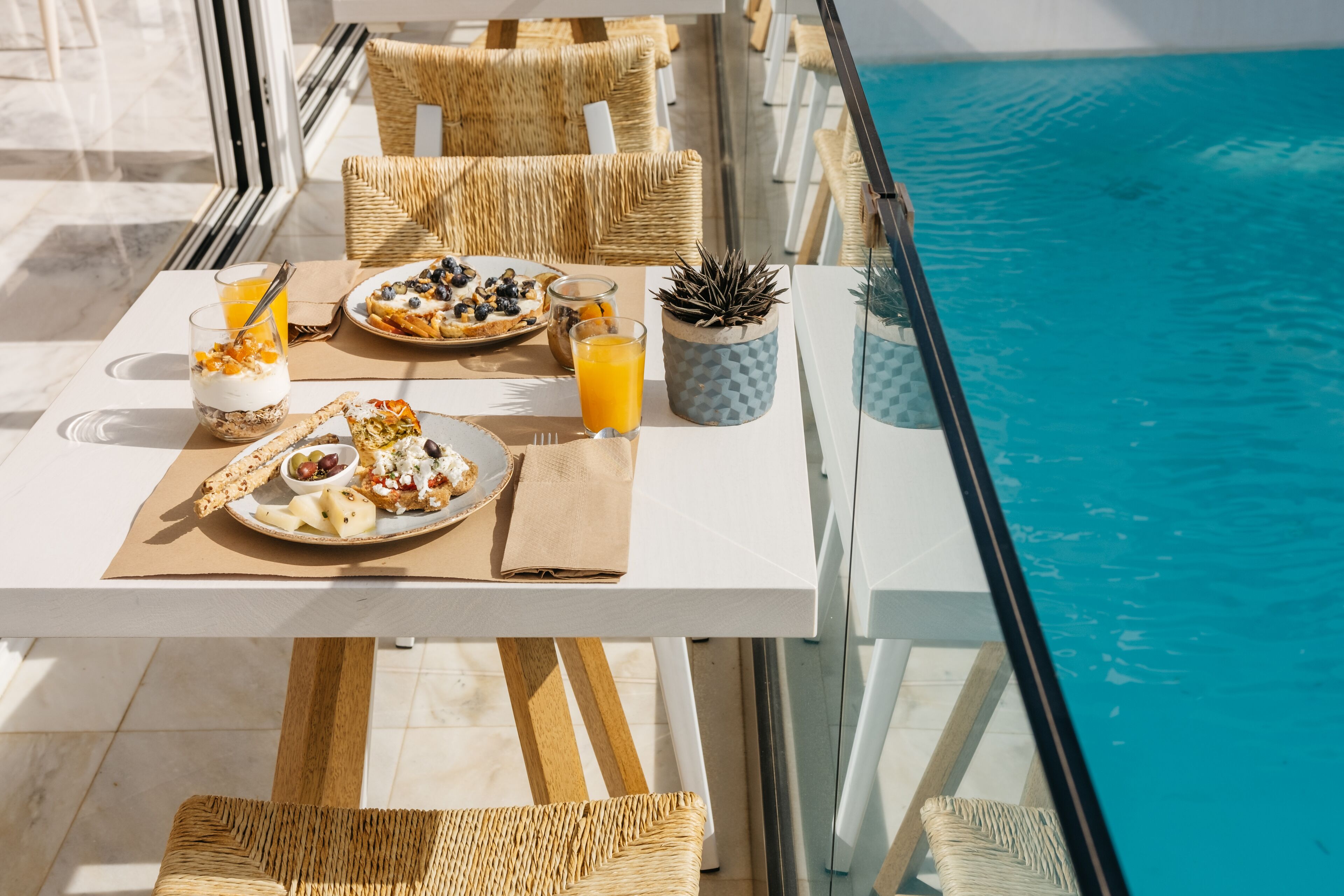 A dining table with breakfast items, wicker chairs, and a view of the pool.