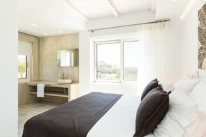 A modern bedroom with a large bed, a bathroom with a sink and mirror, and a window with curtains. - Cyano Hotel (Agios Vasileios)