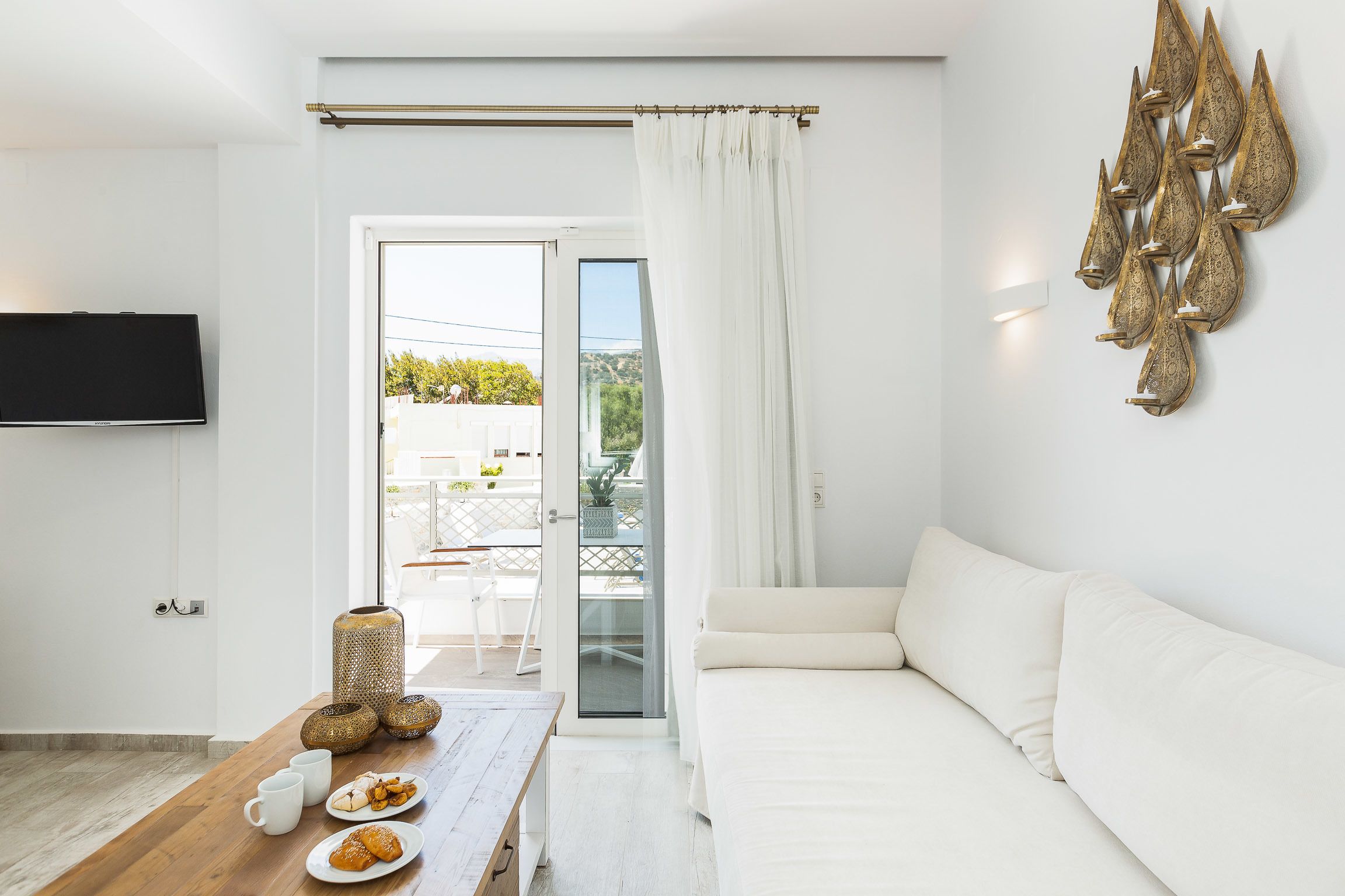 A modern living room with a sofa, a wooden table with a tray of pastries, and a decorative wall piece.
