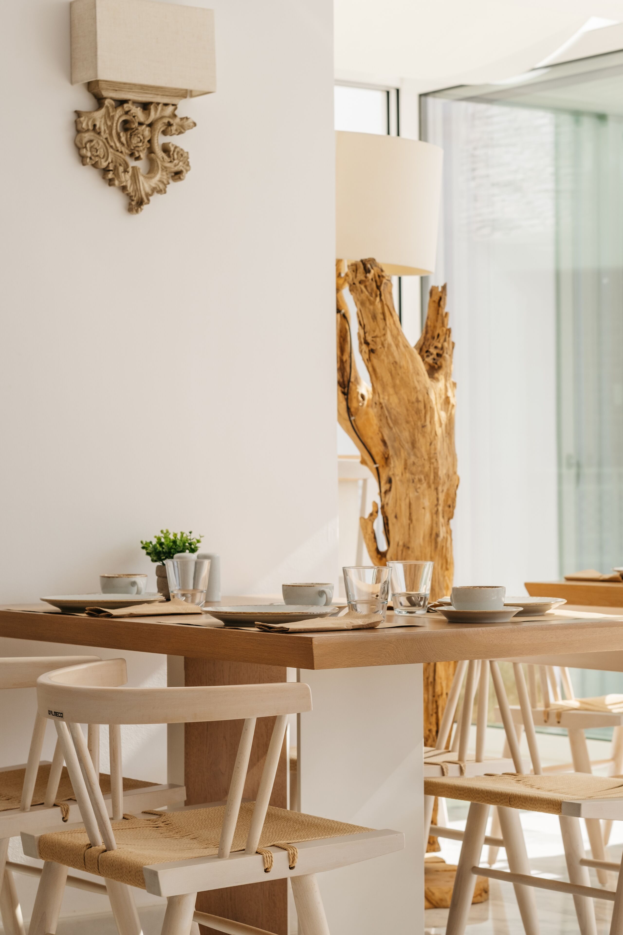 A modern dining area with a wooden table, white chairs, and a large piece of driftwood.