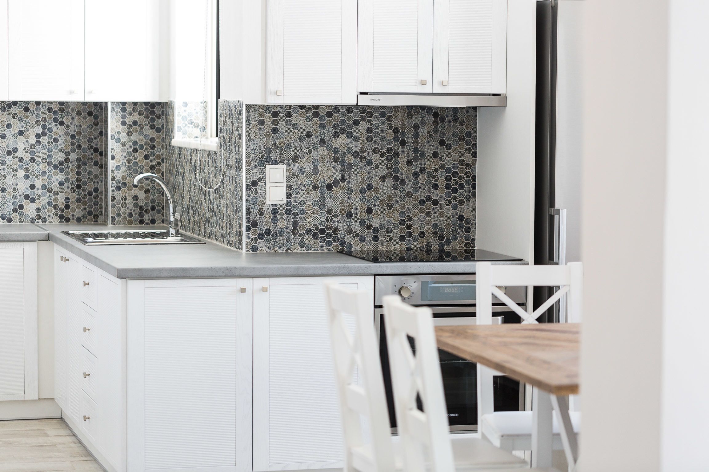 Una cocina moderna con armarios blancos, un lavamanos de acero inoxidable y un salpicadero decorativo.