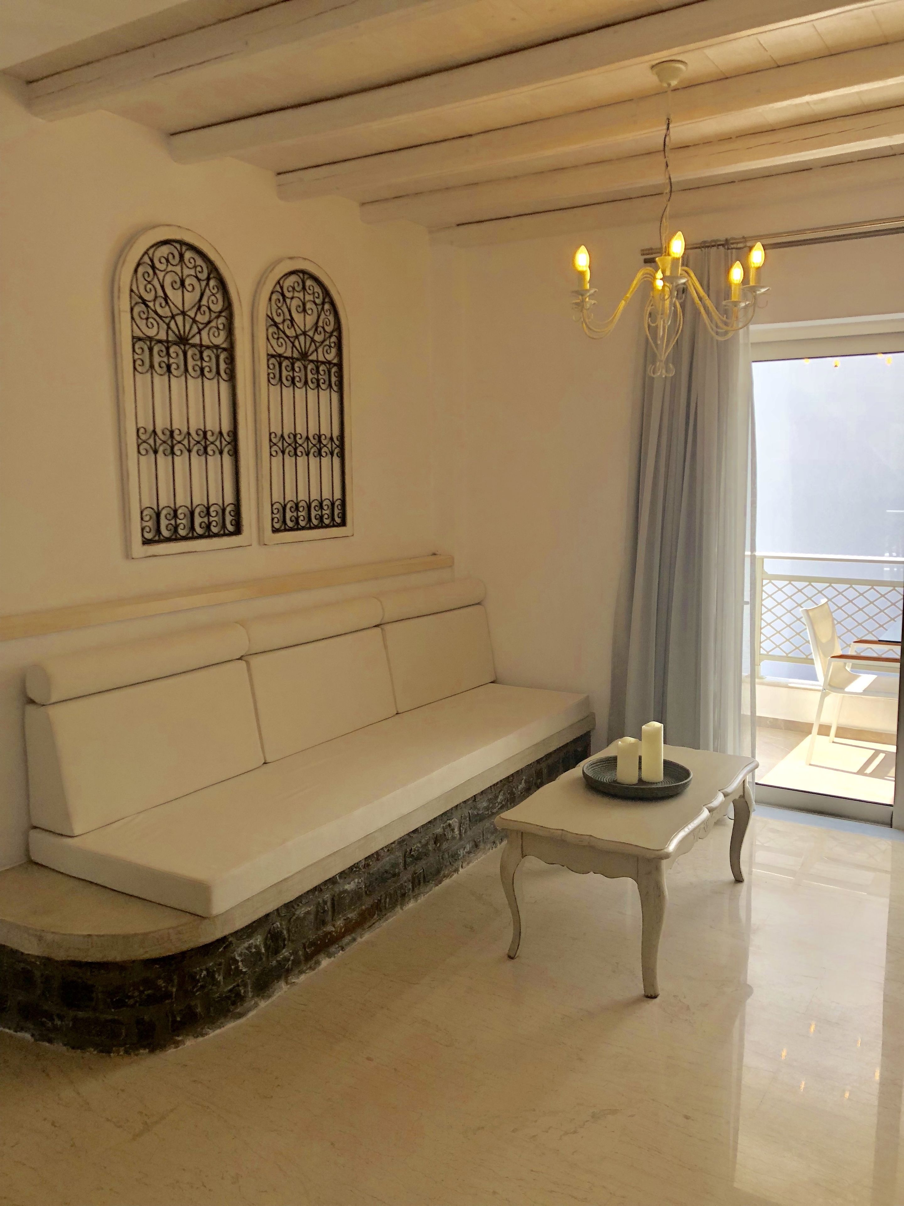 Un salon moderne avec un canapé blanc, une petite table avec des bougies et un balcon offrant une vue agréable.