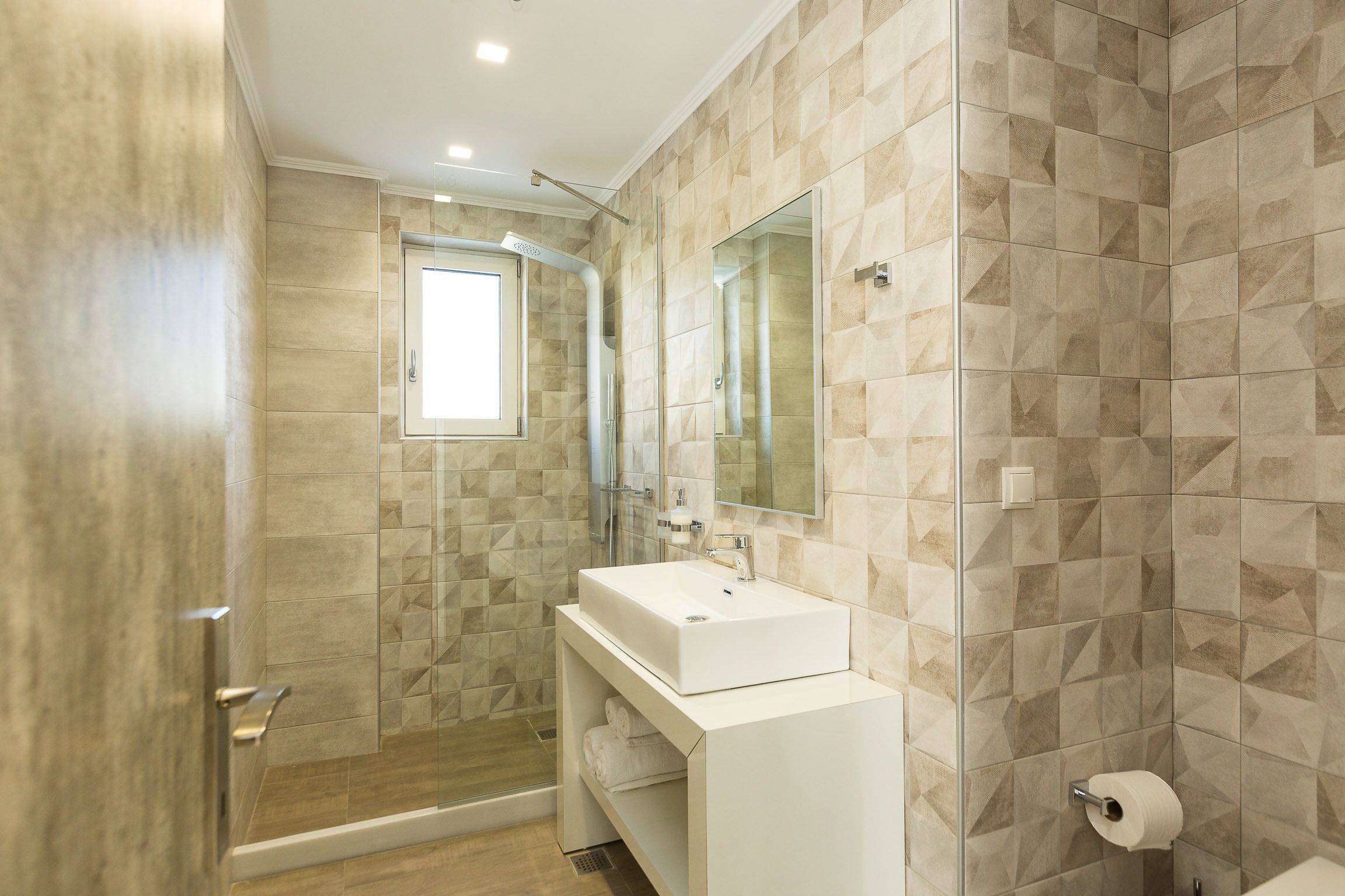 Une salle de bain moderne avec une douche à l’italienne, un grand miroir et un lavabo blanc.