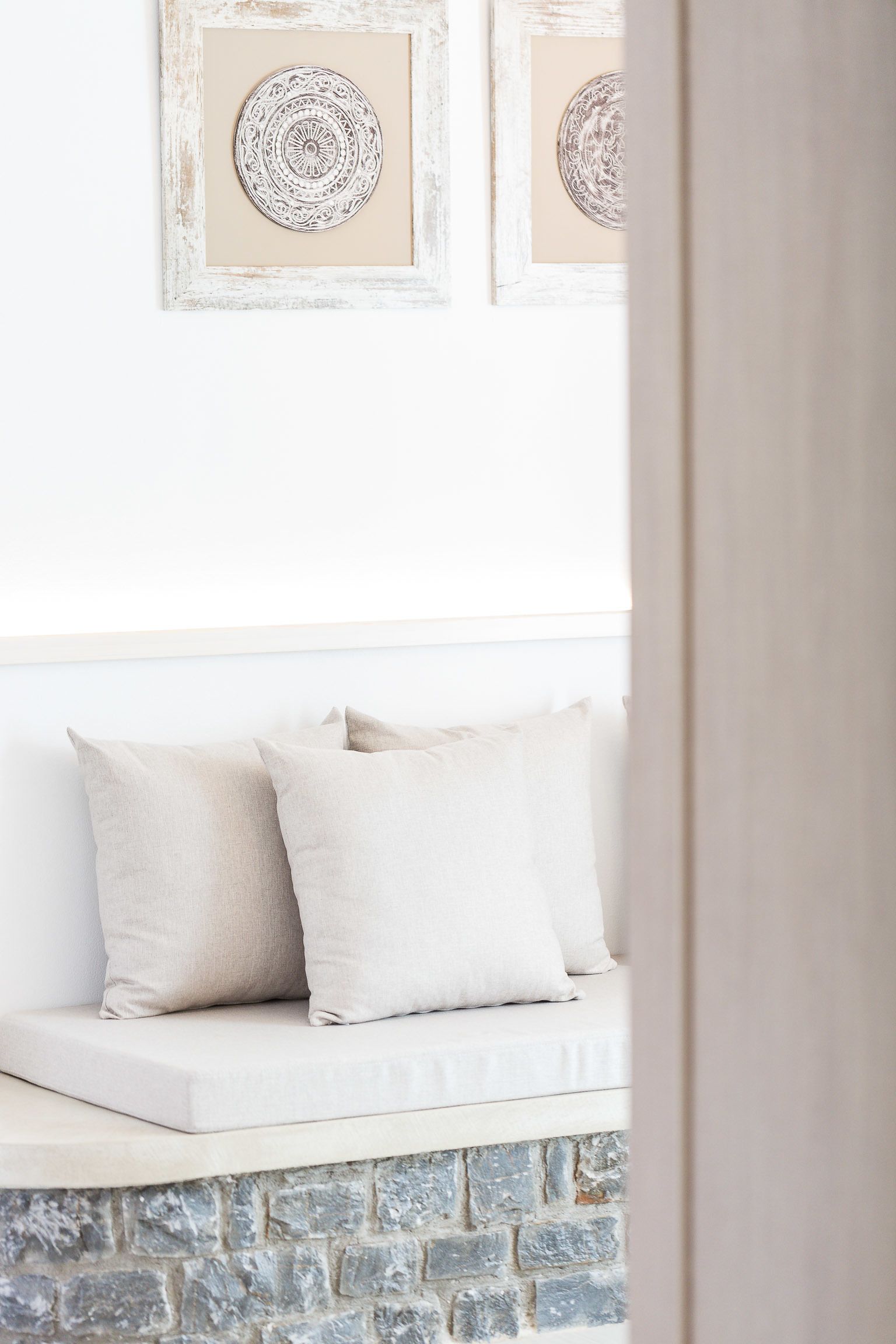 Un banco blanco acolchado con dos almohadones frente a una pared con dos cuadros enmarcados.