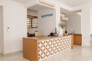 A reception area with a wooden desk, a phone, and a plant. - Cyano Hotel (Agios Vasileios)