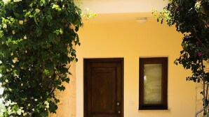 A house entrance with a wooden door, a window, and a small set of steps leading to a door mat. - Angelos Junior Villa with pool HG22 (Kouklia)