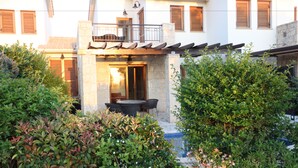 A two-story building with a stone facade, a balcony with a railing, and a patio area with a table and chairs. - Angelos Junior Villa with pool HG22 (Kouklia)