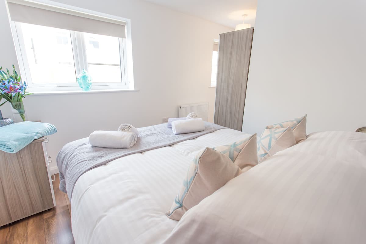 A hotel room with a bed, a bedside table, a window, and a view of the outside.