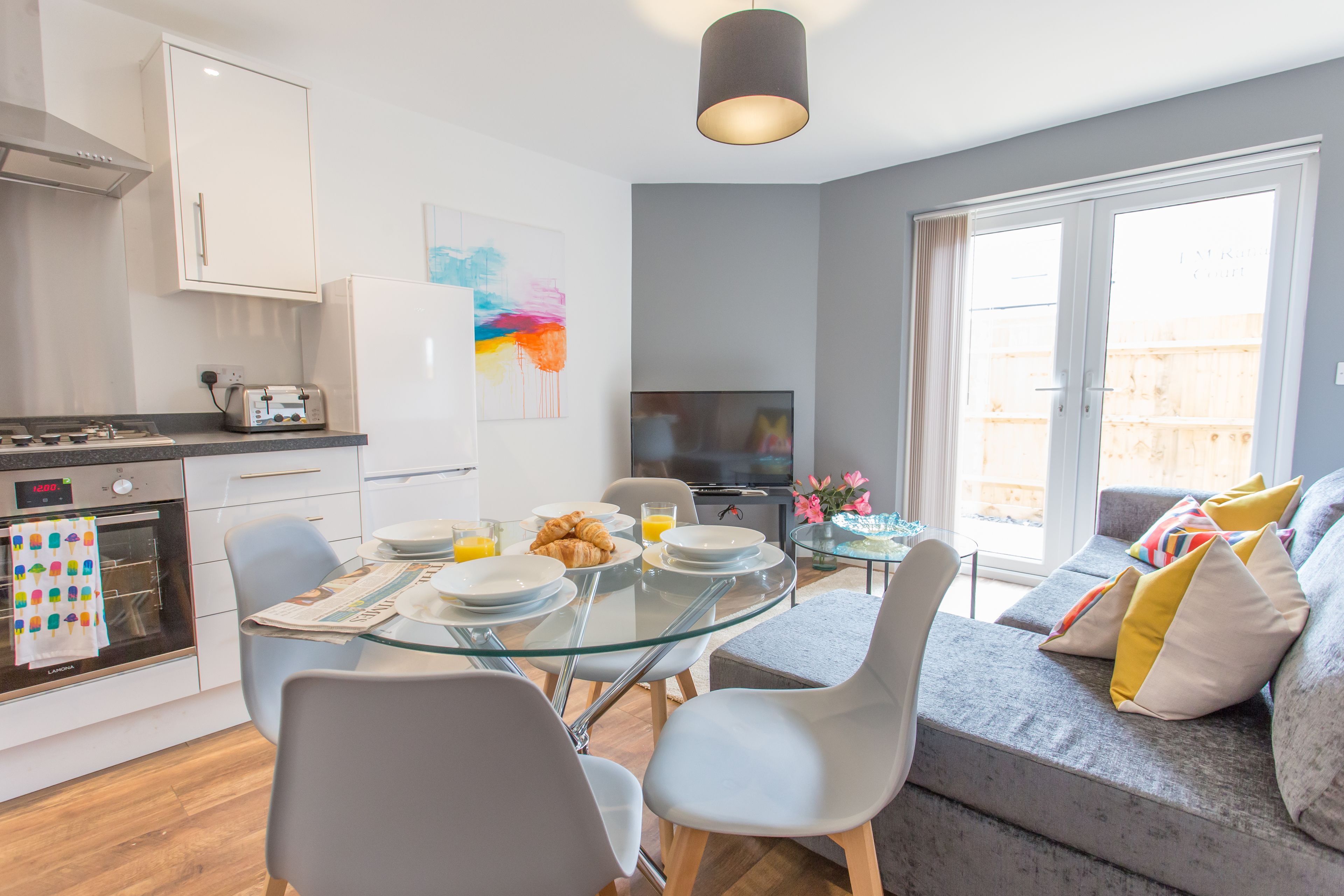 A modern kitchen with a dining area, a sofa, and a TV.