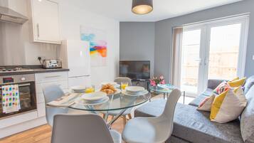 A modern kitchen with a dining area, a sofa, and a TV.