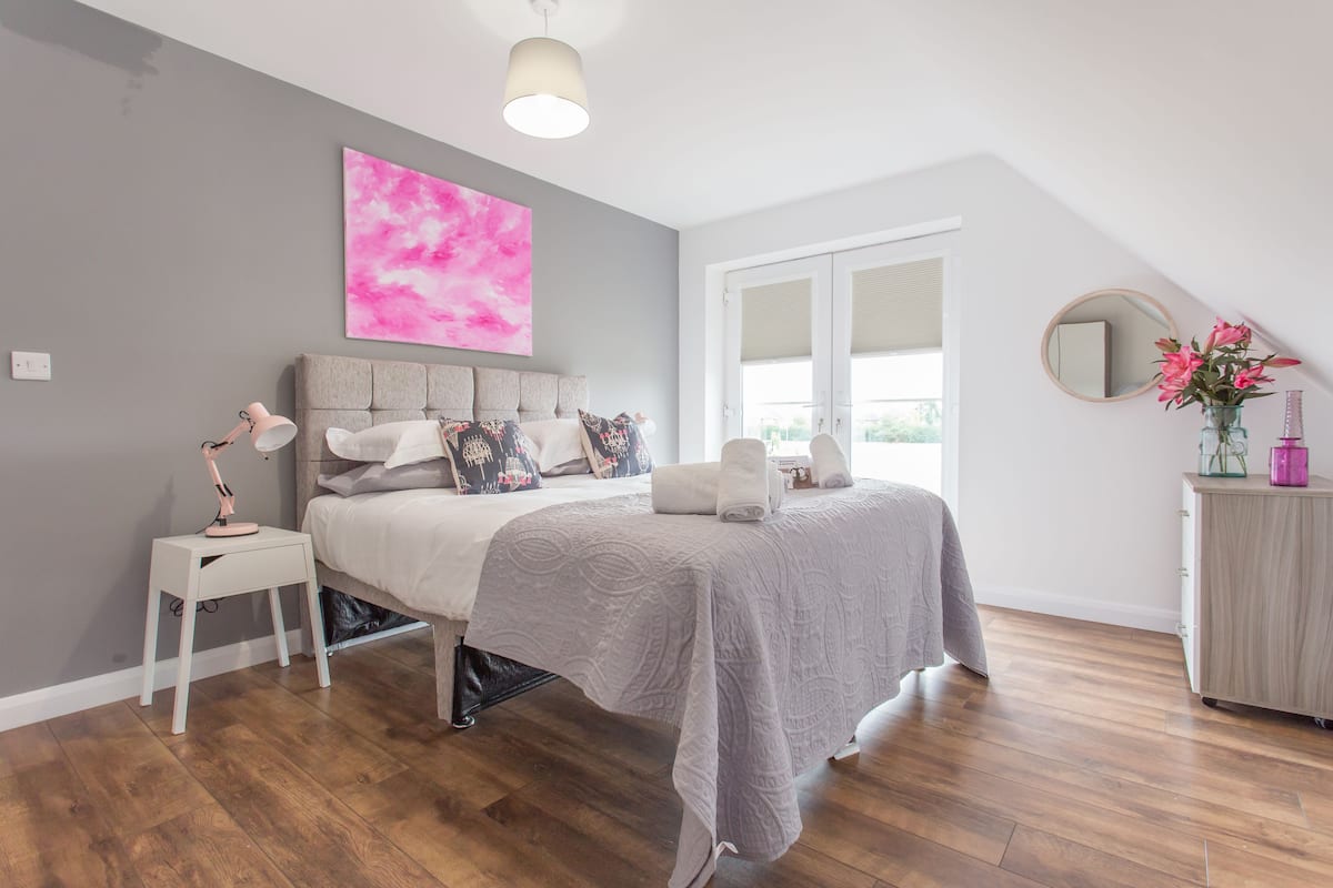 A bedroom with a bed, bedside table, lamp, and a large window.