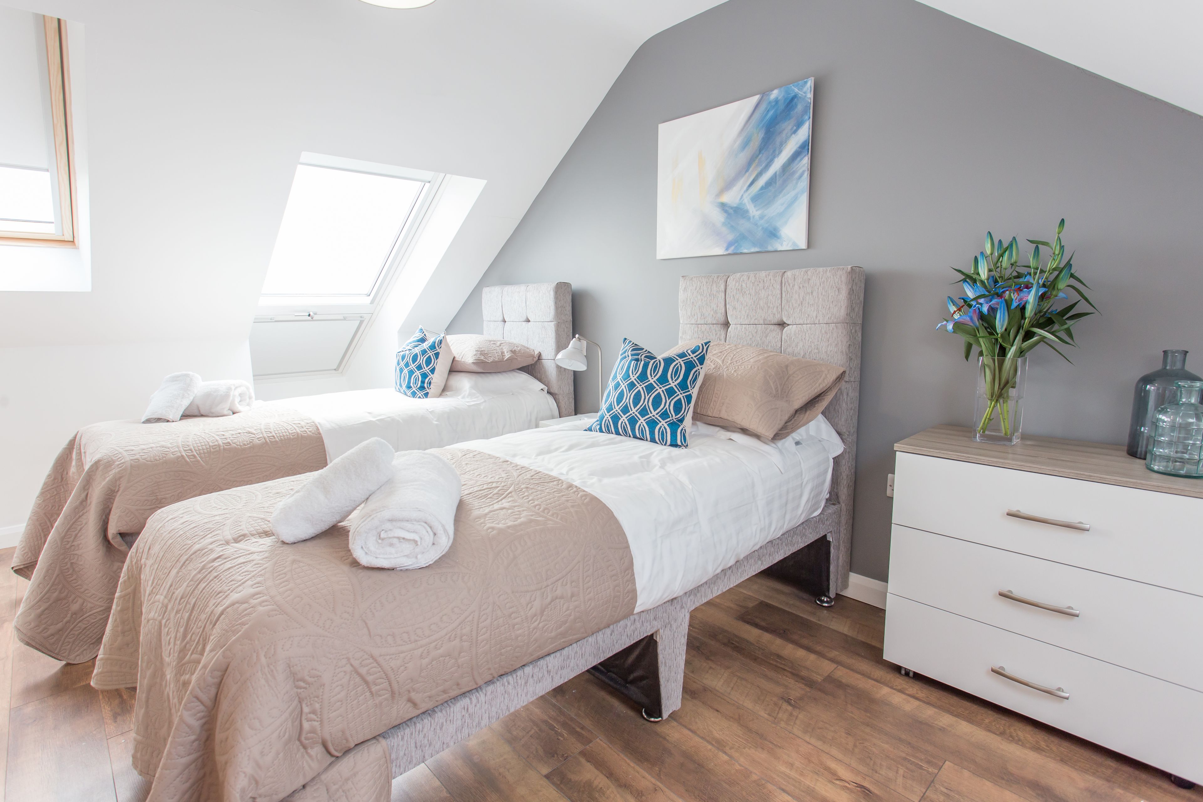 Una camera da letto moderna con due letti, un lucernario, un grande quadro astratto e un vaso con fiori.