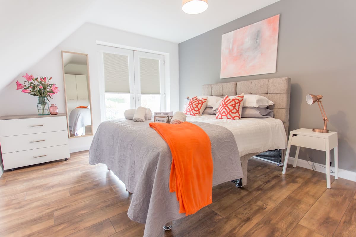 A bedroom with a bed, a dresser, a mirror, a lamp, and a painting on the wall.