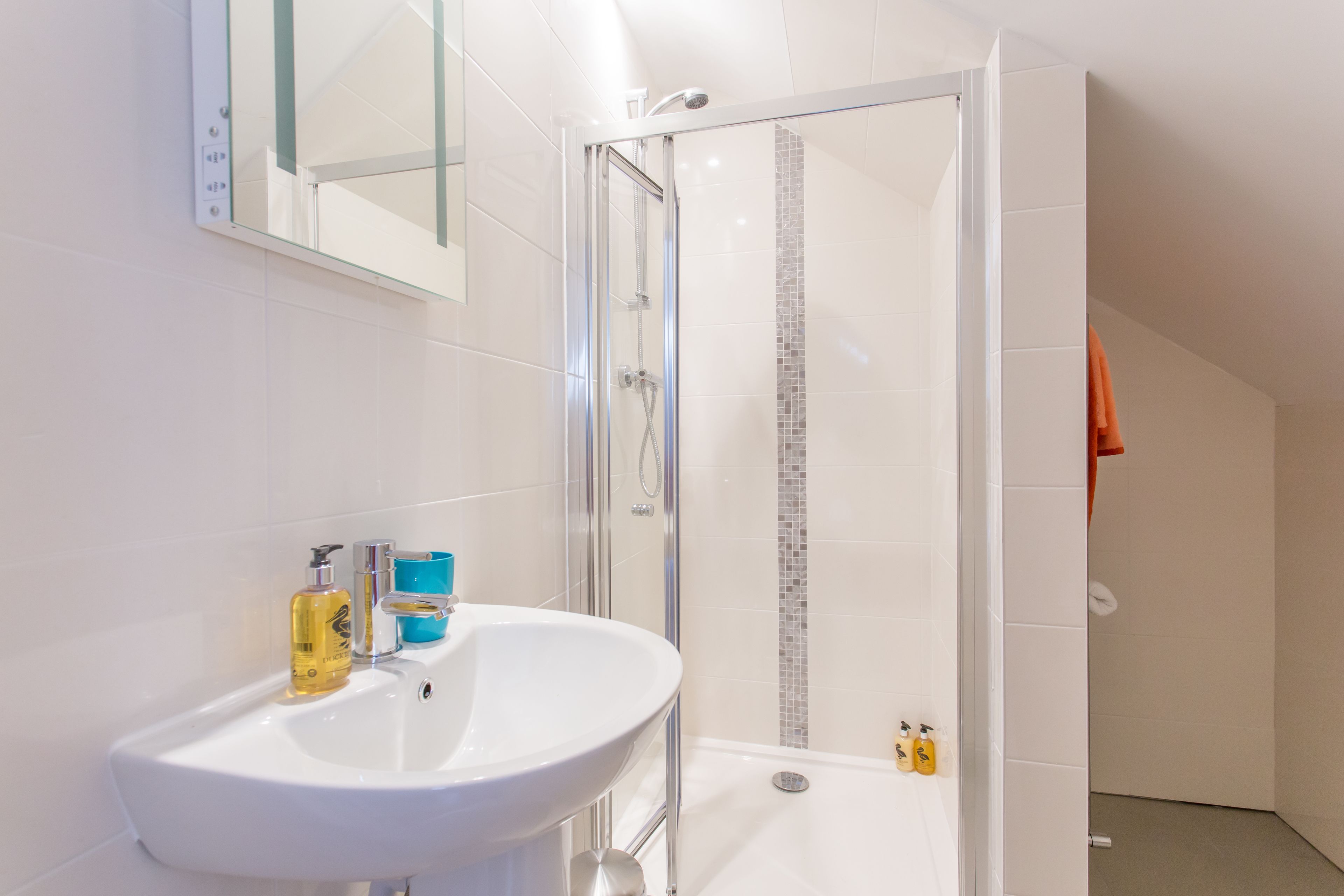 A modern bathroom with a white sink, glass shower enclosure, and tiled walls.