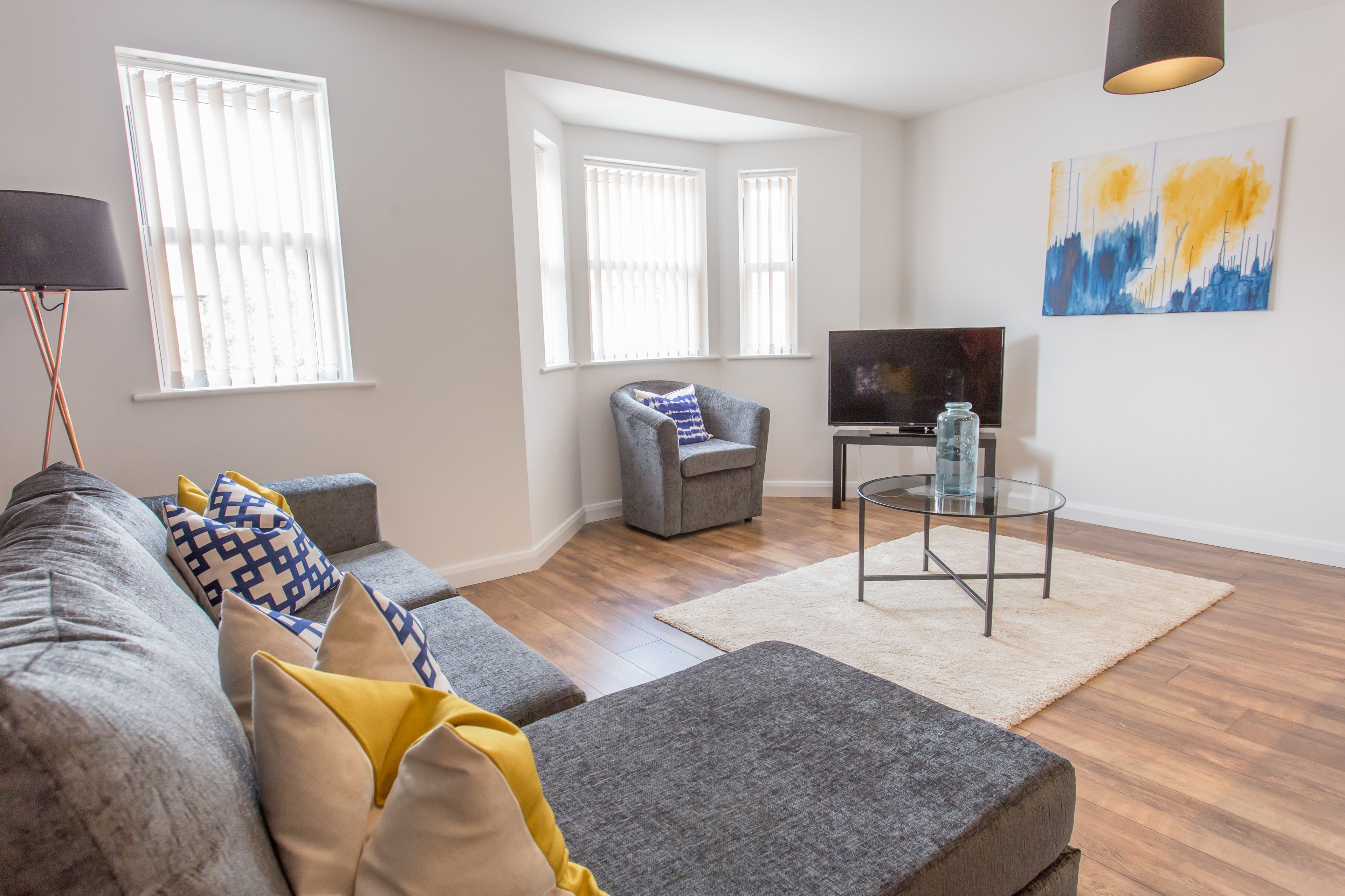 A living room with a sofa, ottoman, and armchair, a TV, and a glass coffee table.