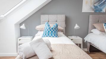 A modern bedroom with a sloped ceiling, two bedside tables, a large bed with patterned bedding, and a blue and white pillow.