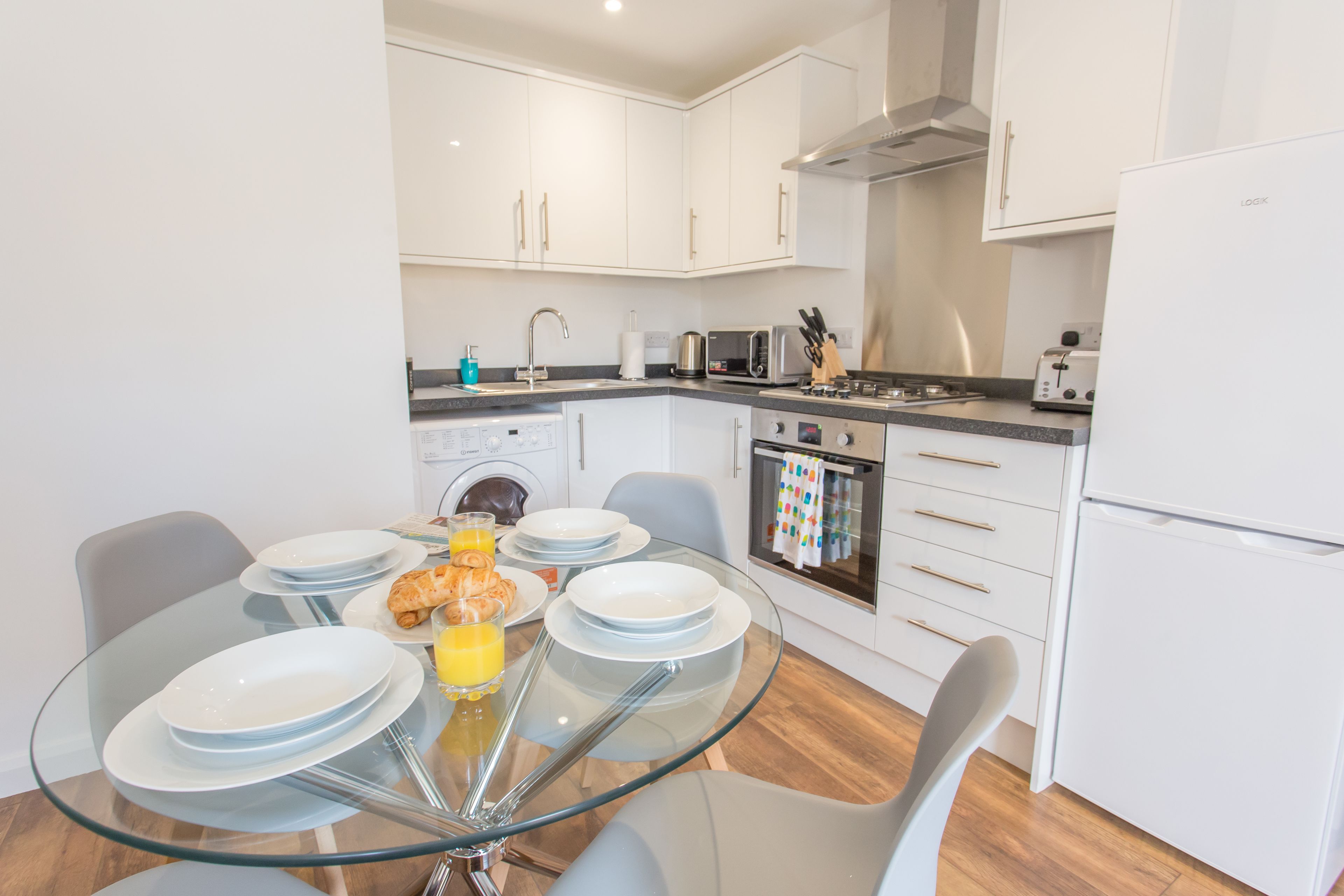 Una cocina moderna con gabinetes blancos, una mesa de comedor de vidrio y un horno empotrado.