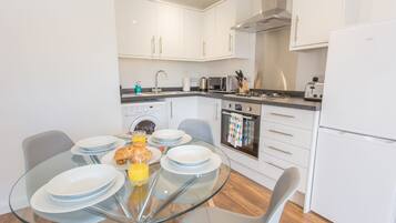 A modern kitchen with white cabinets, a glass dining table, and a built-in oven.