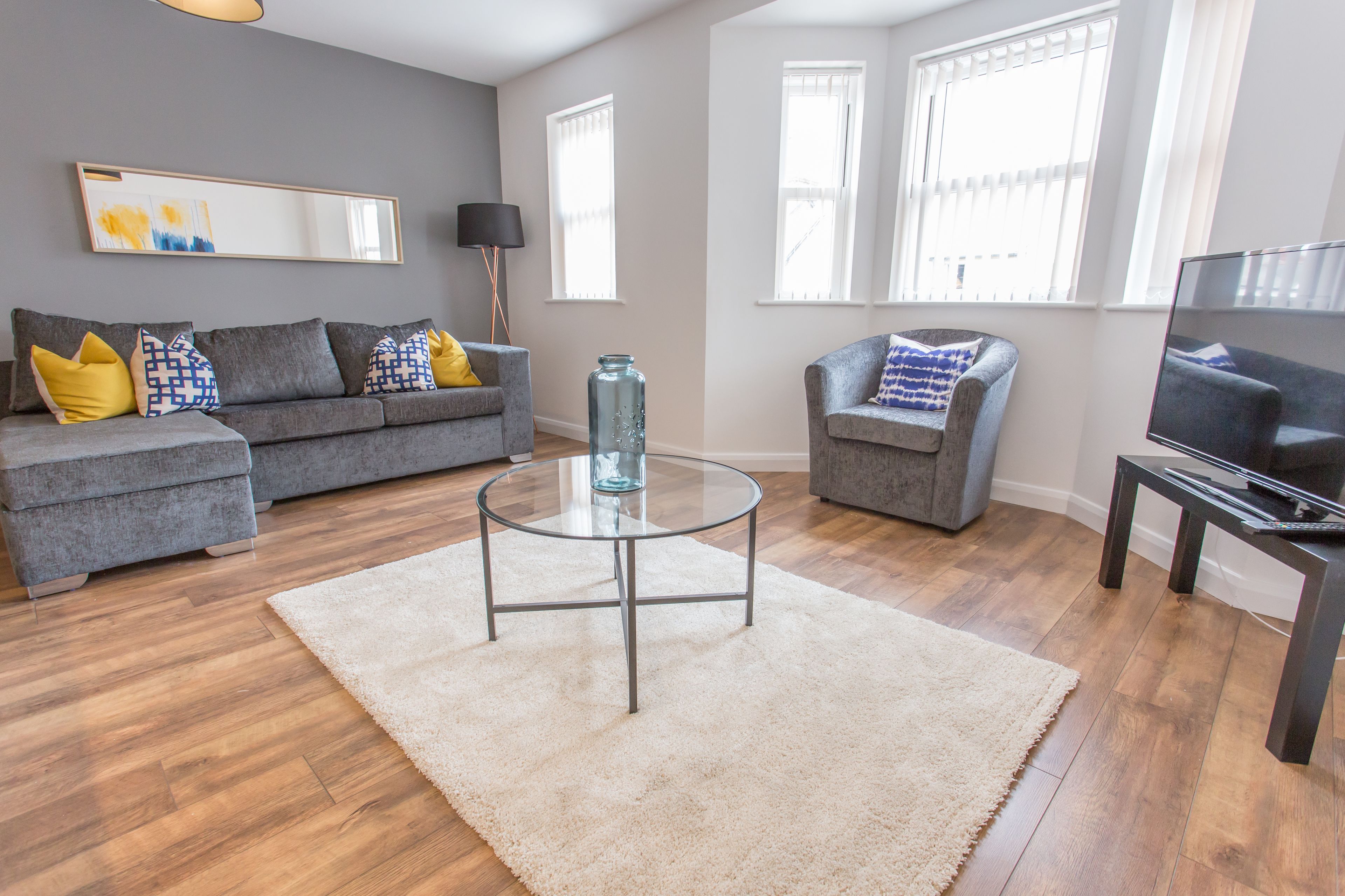 A modern living room with a grey sofa, a glass coffee table, and a TV stand.