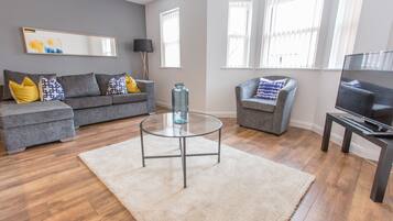 A modern living room with a grey sofa, a glass coffee table, and a TV stand.