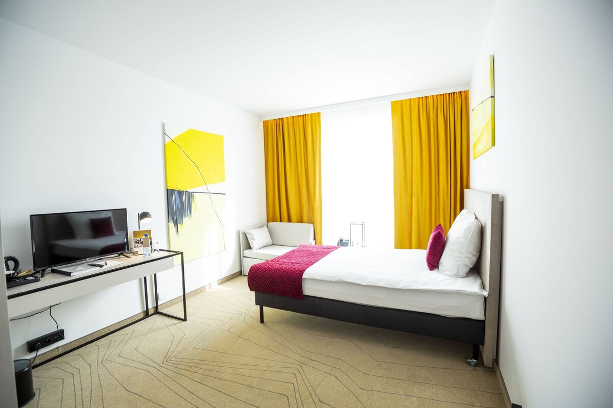 A hotel room with a bed, a desk with a TV, and a chair.