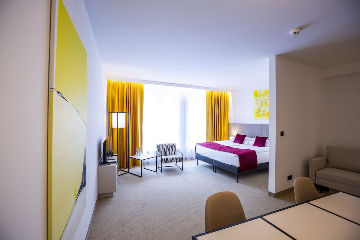 A hotel room with a bed, a desk, a chair, and a sofa.