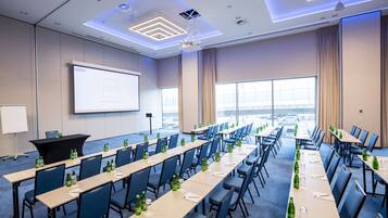 A conference room with long tables, chairs, and a projector screen.