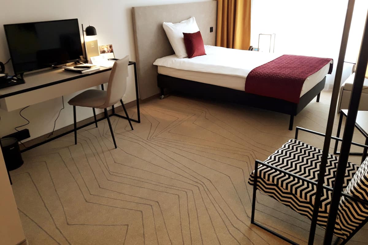 A hotel room with a bed, a desk with a computer, a chair, and a TV.
