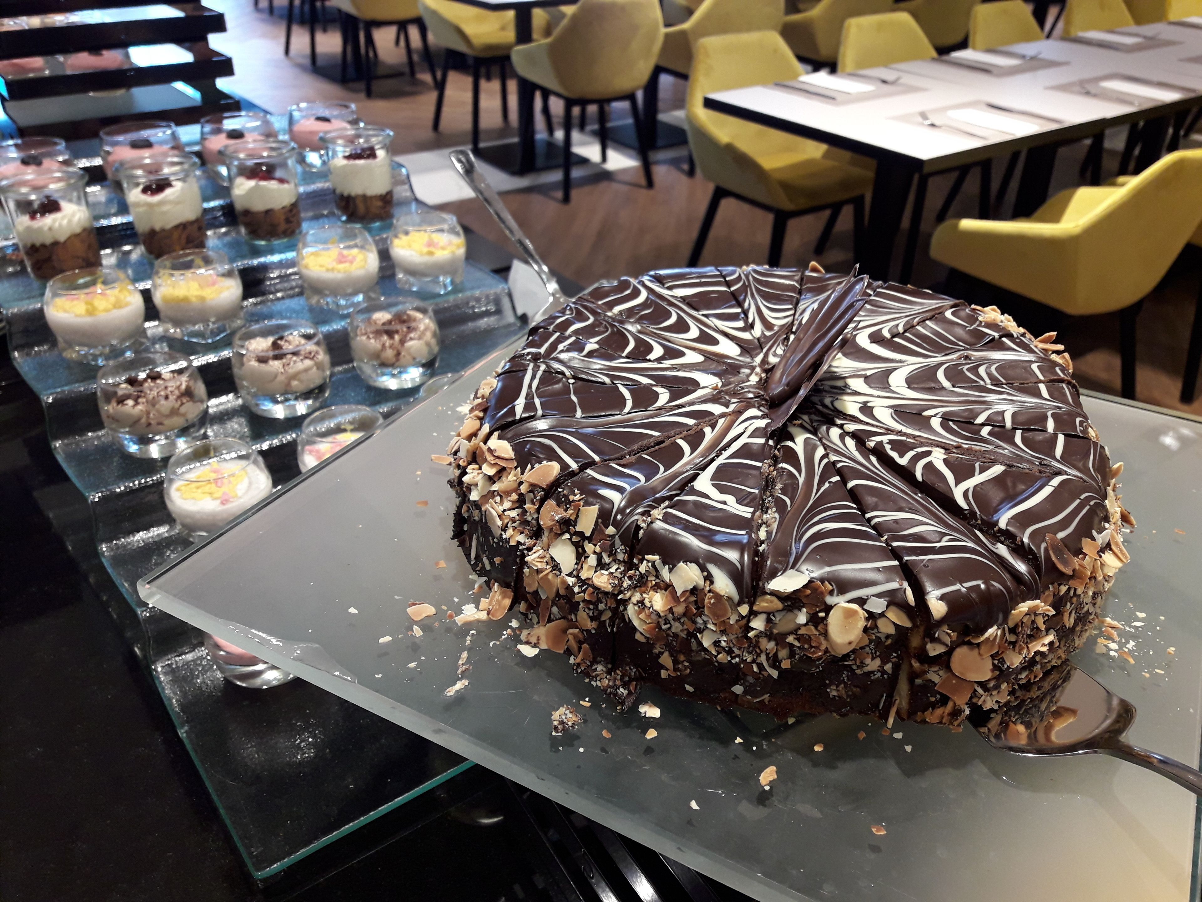 A dessert display with a chocolate-covered cake and various small desserts on a glass tray.