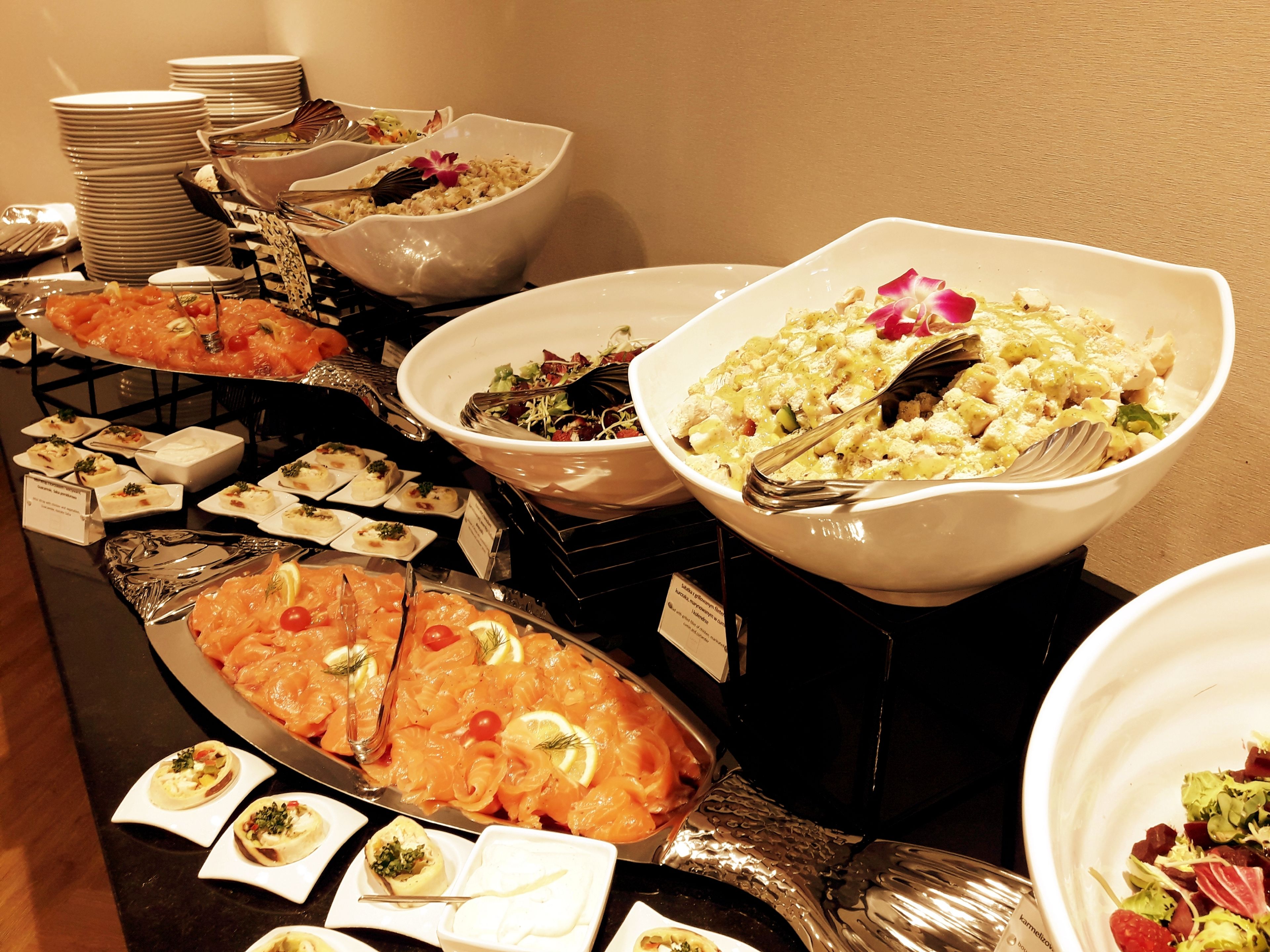 Um buffet com diversos pratos, incluindo salmão e saladas, dispostos sobre uma mesa.