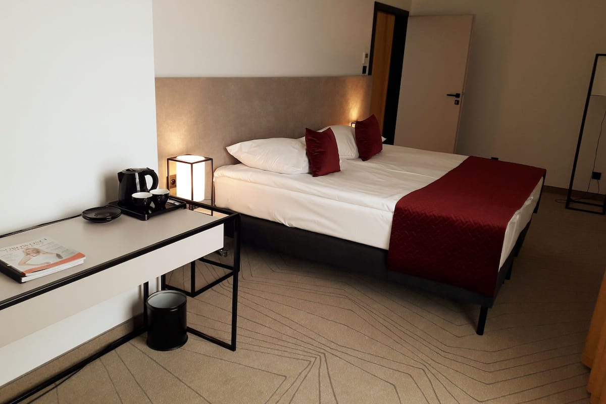 A hotel room with a bed, bedside table, lamp, and a magazine.