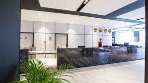 A modern hotel reception area with a marble counter, a receptionist, and a view of the lobby. - Arche Hotel Krakowska (Warsaw)