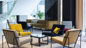 A modern lobby with a central seating area, a staircase, and a large window providing a view of the city. - Arche Hotel Krakowska (Warsaw)