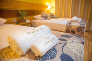 Zwei ordentlich gefaltete weiße Handtücher mit dem Aufdruck "COPASU HOTEL", platziert auf einem Bett mit einem blumigen Kissen.