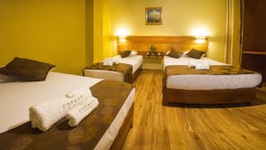 Ein Hotelzimmer mit zwei Betten, jeweils mit einem hölzernen Kopfteil und einer blumigen Tagesdecke. Auf jedem Bett liegen zwei Handtücher mit dem Schriftzug 'COPASU'. Der Raum verfügt über einen Holzboden und ein Bild an der Wand über den Betten.