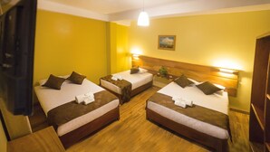 Habitación de hotel con tres camas individuales, cada una con cabecero de madera, ropa de cama blanca y almohadones marrones. Hay un cuadro en la pared y una planta pequeña en la mesita de noche.