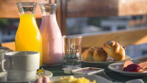 Una mesa de desayuno con un croissant, jamón y piña, junto con dos botellas de jugo y un vaso de agua.